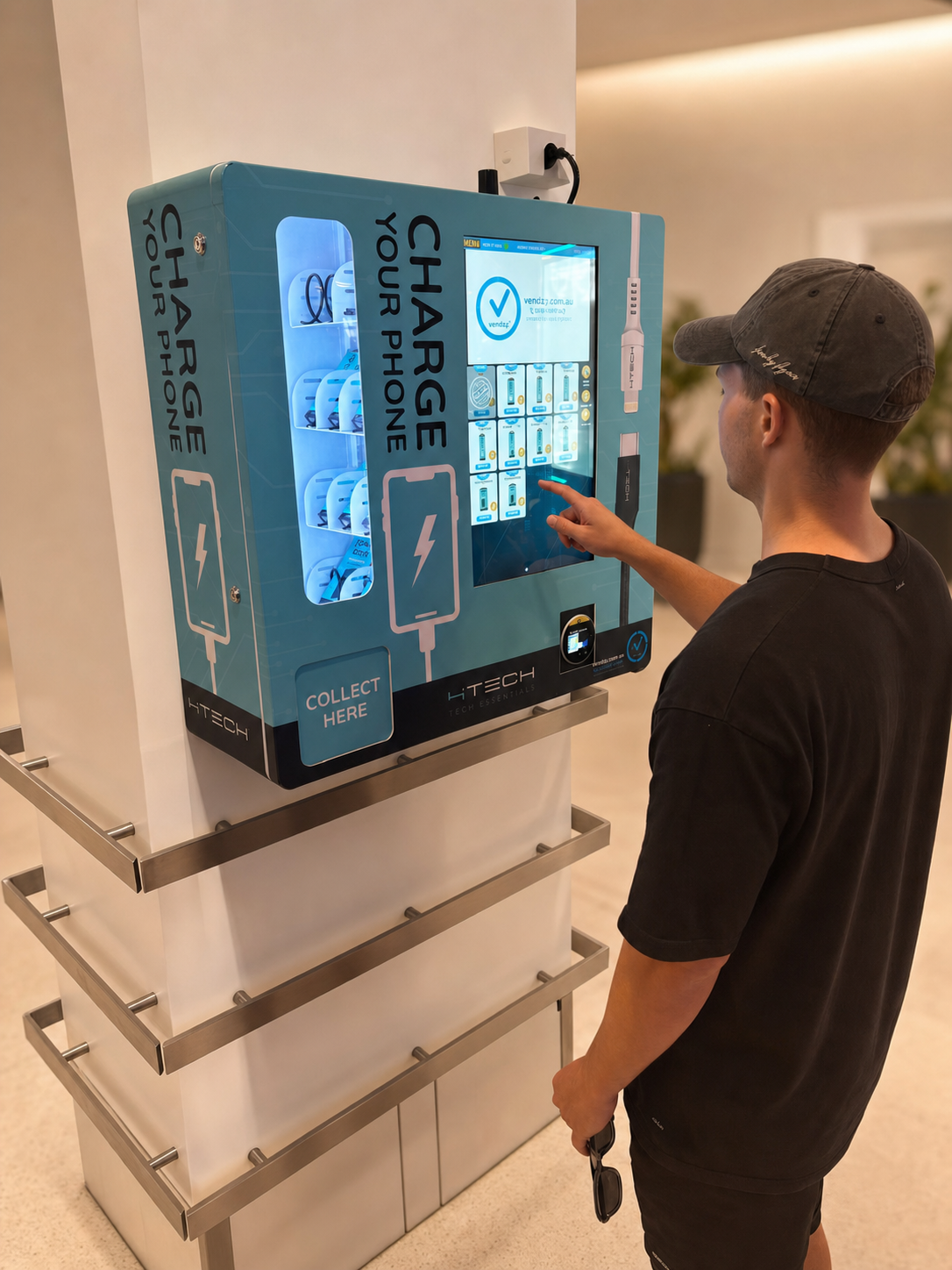 A wall-mounted 4Tech tech-essentials machine in teal branding, reading Charge Your Phone, stocked with USB-C and lightning cables, fast chargers and power banks, with a Collect Here pickup hatch