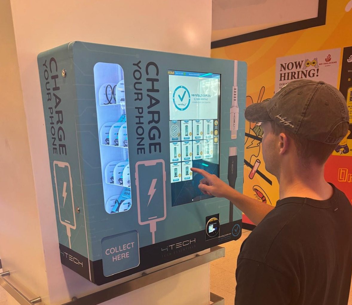 A customer using a wall-mounted teal 4Tech Charge Your Phone machine at a venue